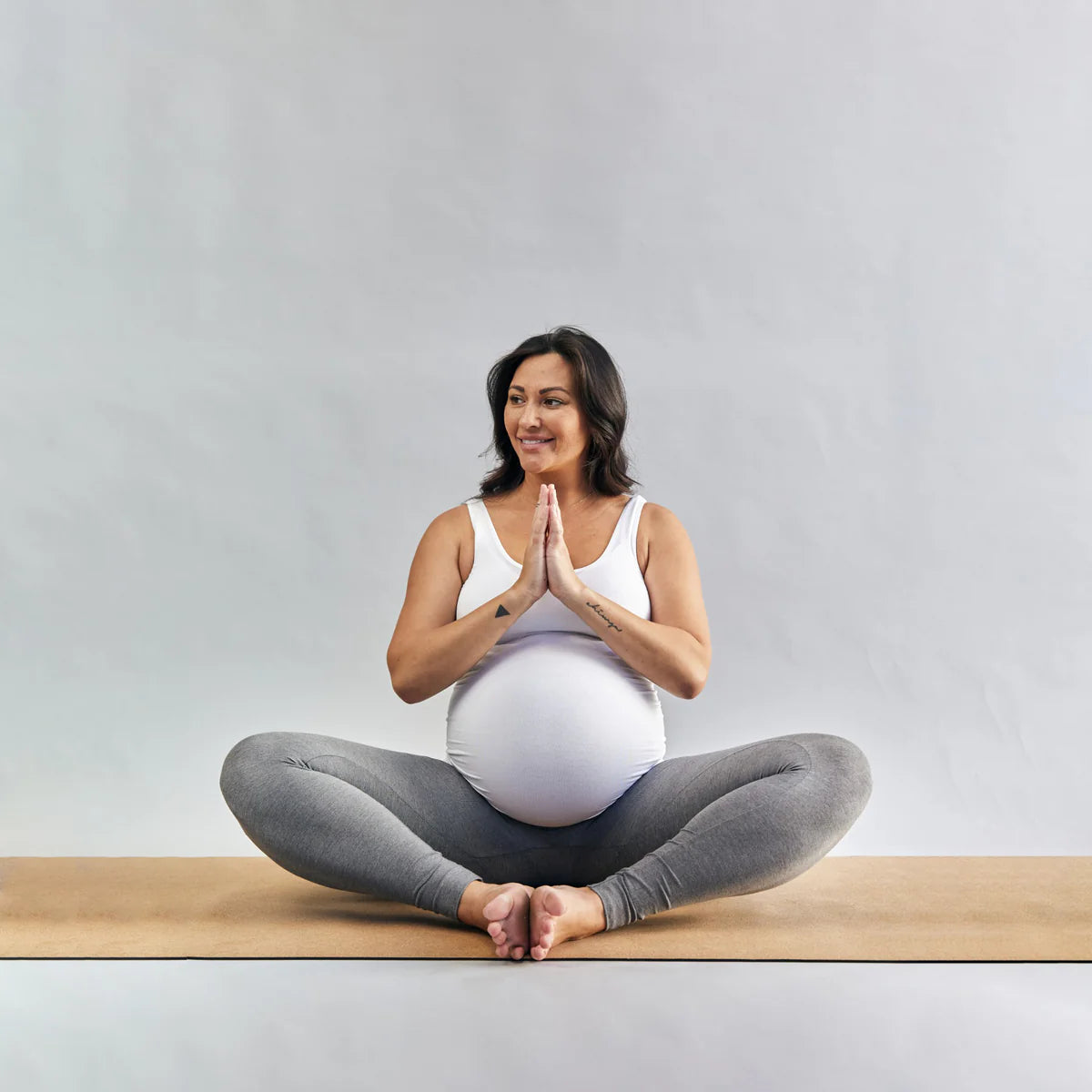 Pregnant woman sitting on a yoga mat with a neutral background
