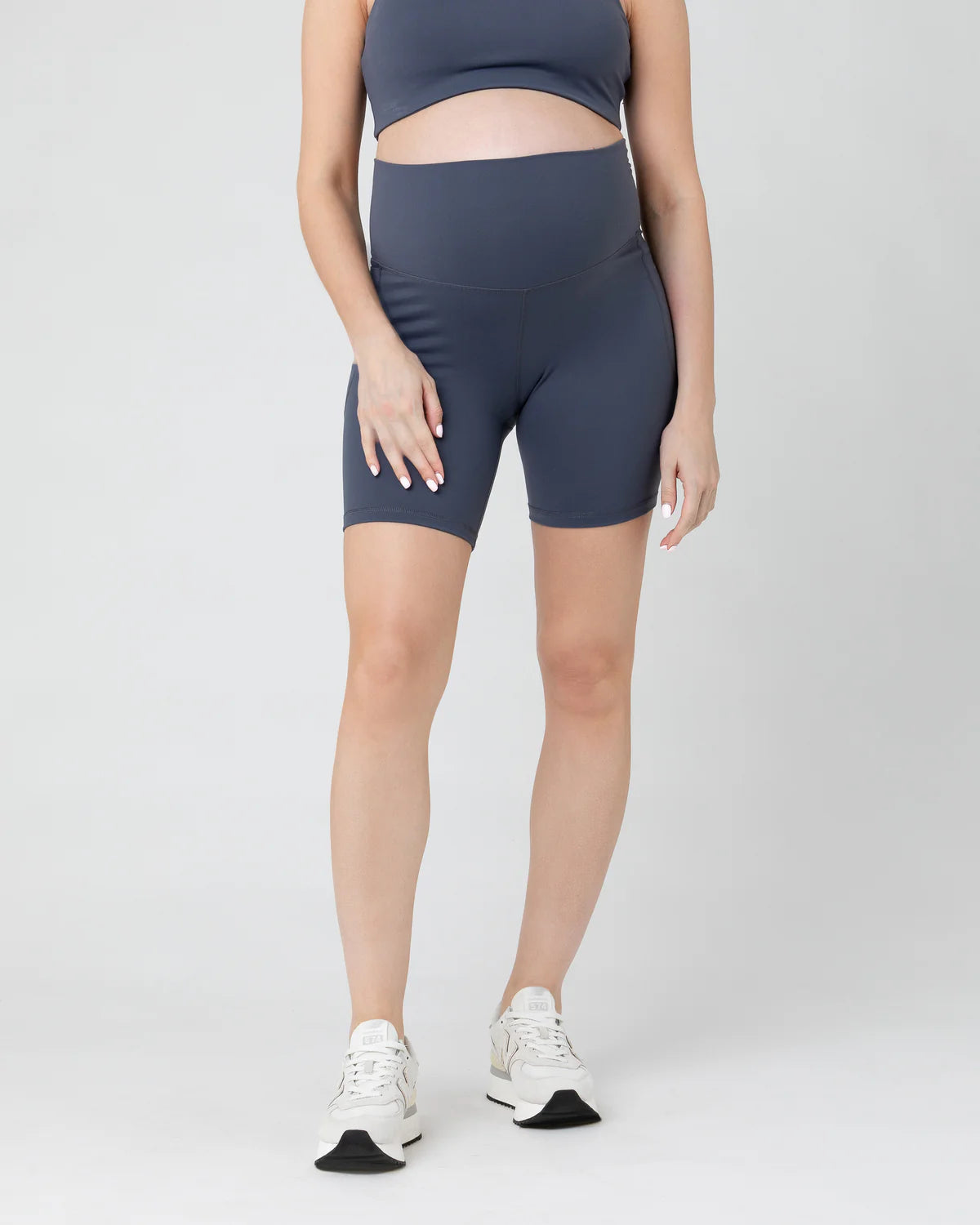 Pregnant woman wearing dark blue athletic shorts on a white background