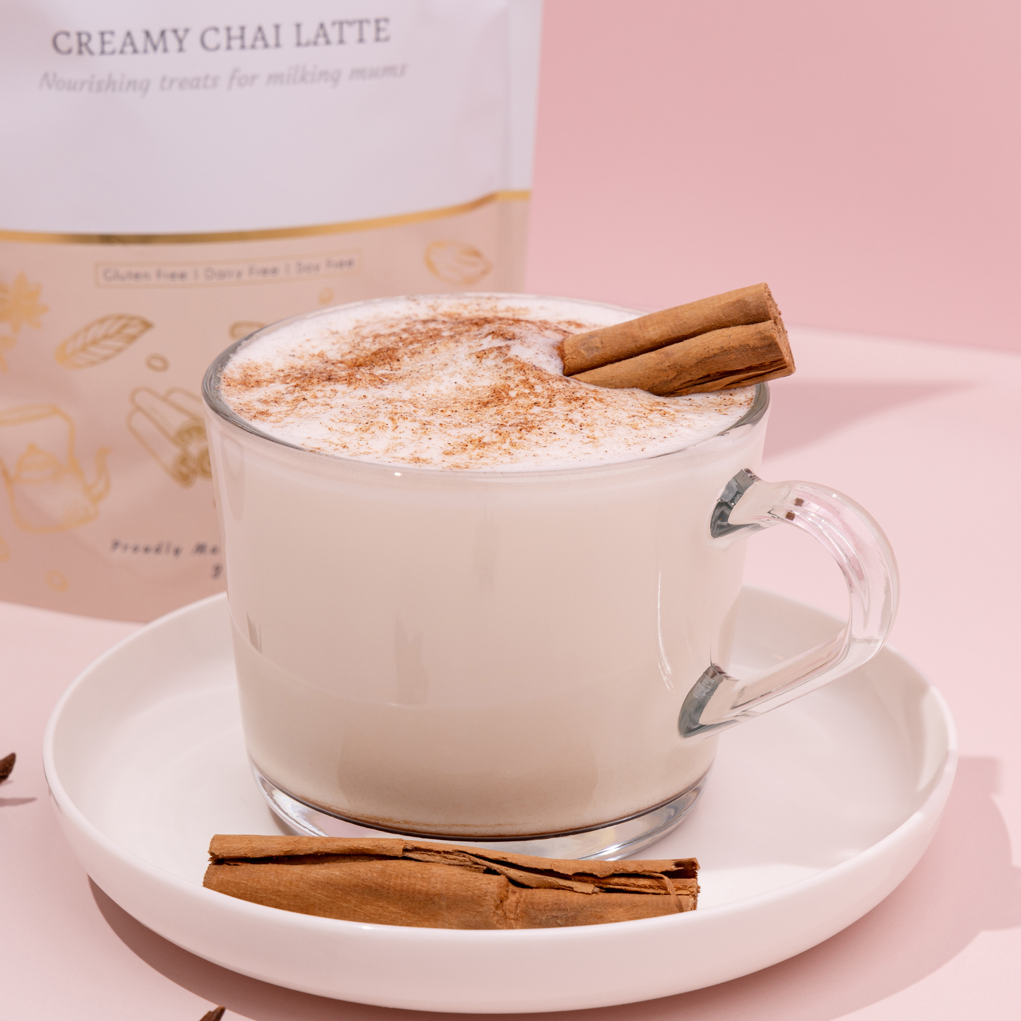 Glass mug of creamy chai latte with cinnamon stick on a pink background
