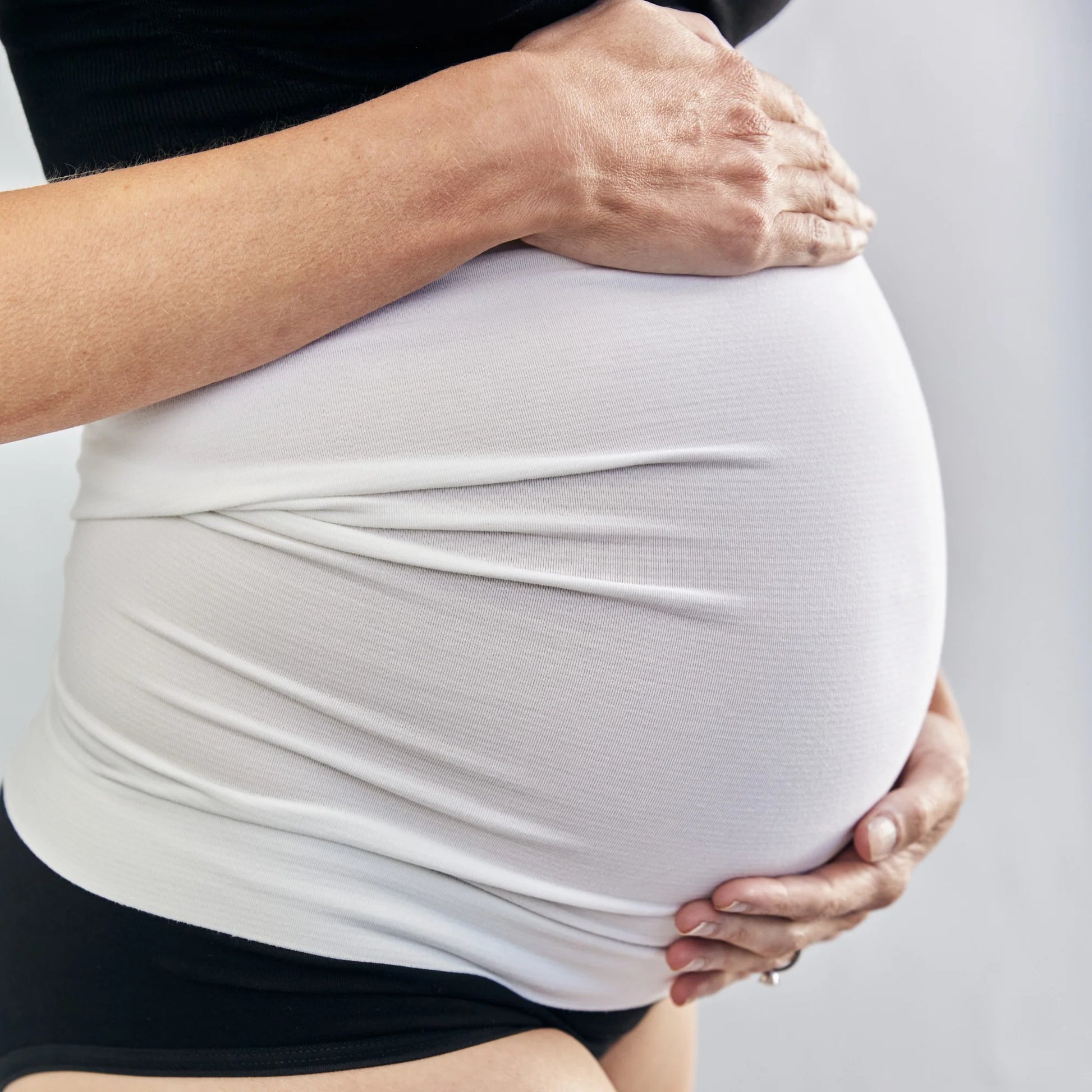 Close-up of a pregnant person holding their belly against a neutral background
