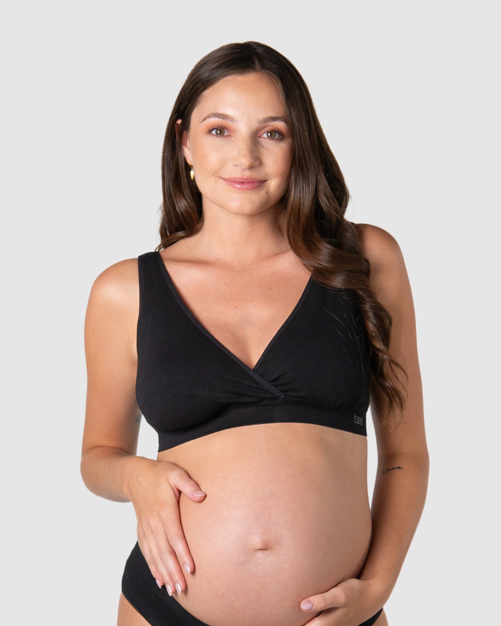 Pregnant woman wearing a black maternity bikini top against a plain background