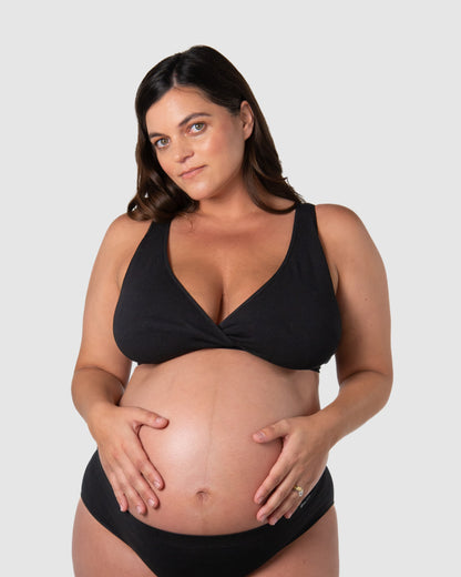 Pregnant woman wearing a black bikini set on a plain background