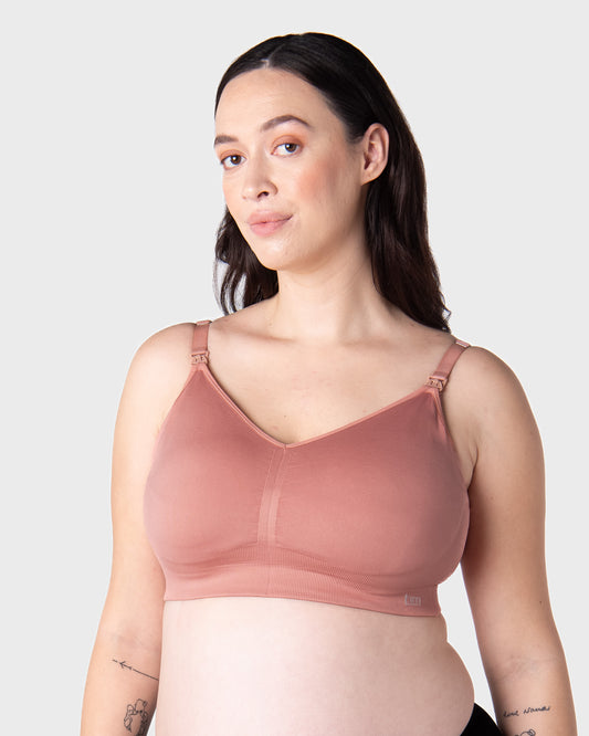 Pregnant Woman wearing a pink nursing bra against a plain background