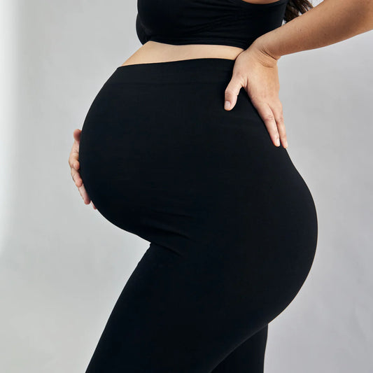 Pregnant person wearing black leggings against a grey background