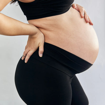 Pregnant person wearing black leggings with a plain background