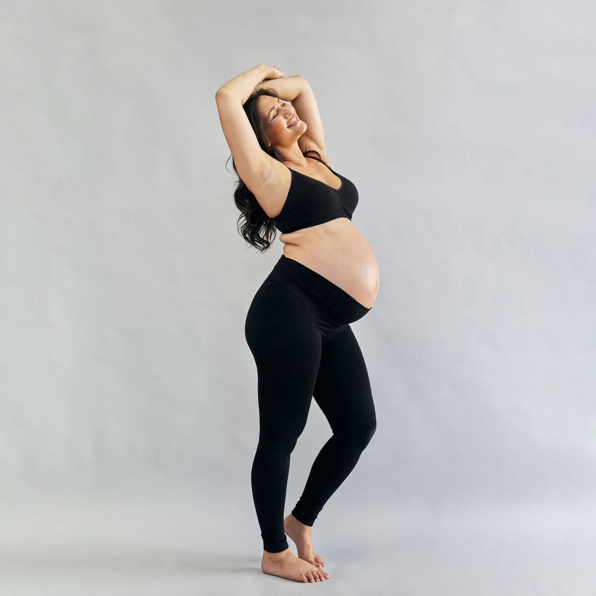 Pregnant woman wearing a black outfit against a grey background