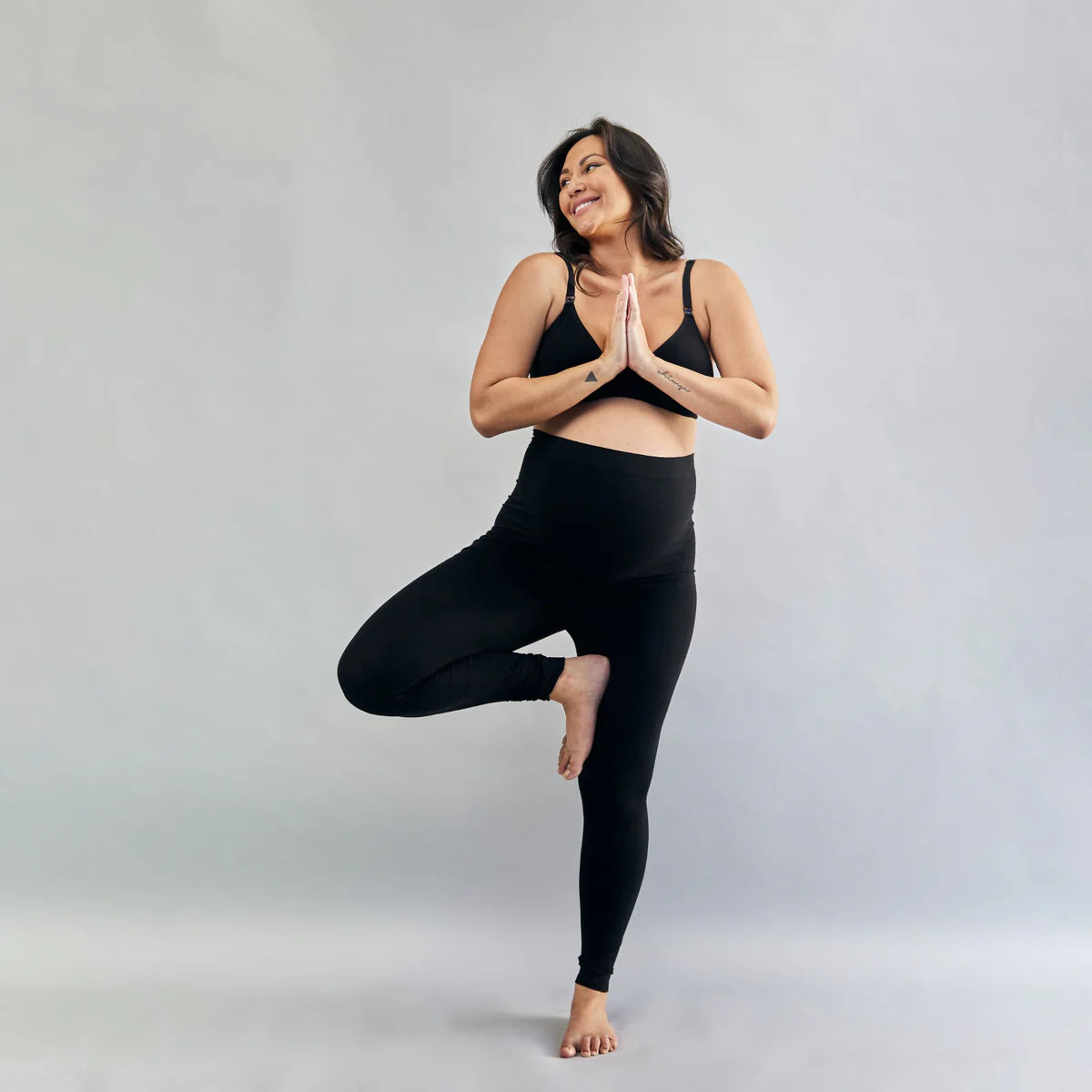 Pregnant Woman in a yoga pose wearing black athletic wear on a grey background