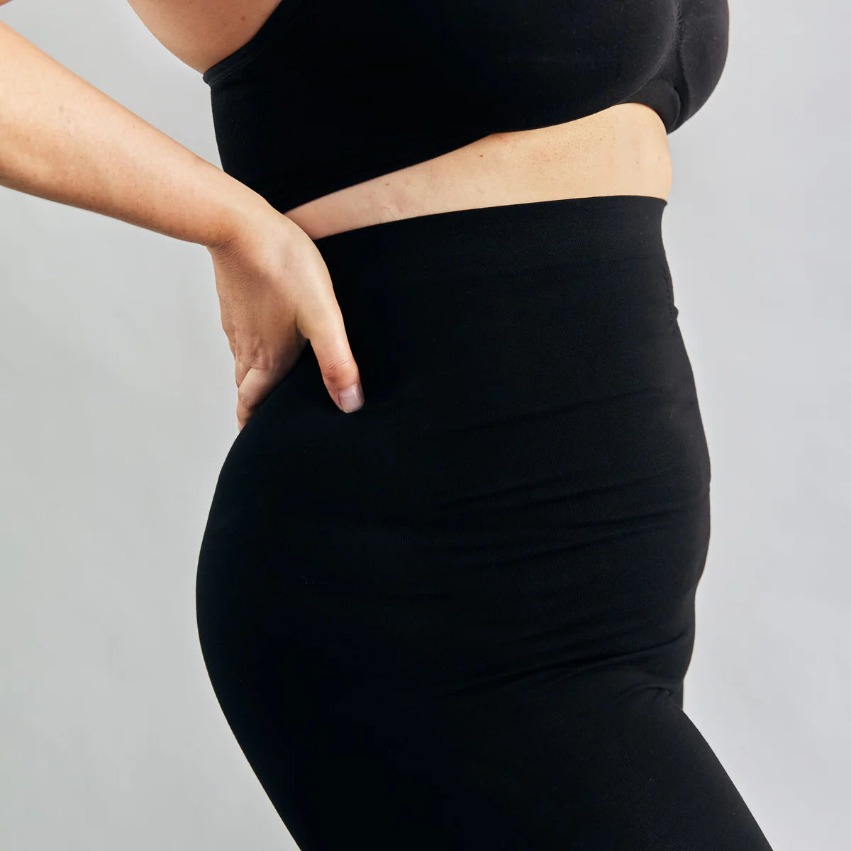 Postpartum woman wearing a fitted black outfit on a plain background
