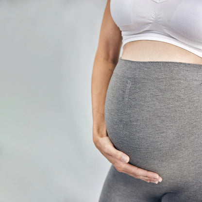 Pregnant Woman wearing grey leggings and a white top on a plain background
