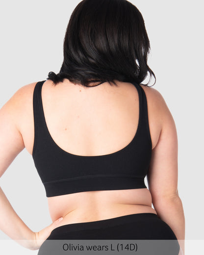 Pregnant woman wearing a black sports bra on a plain background
