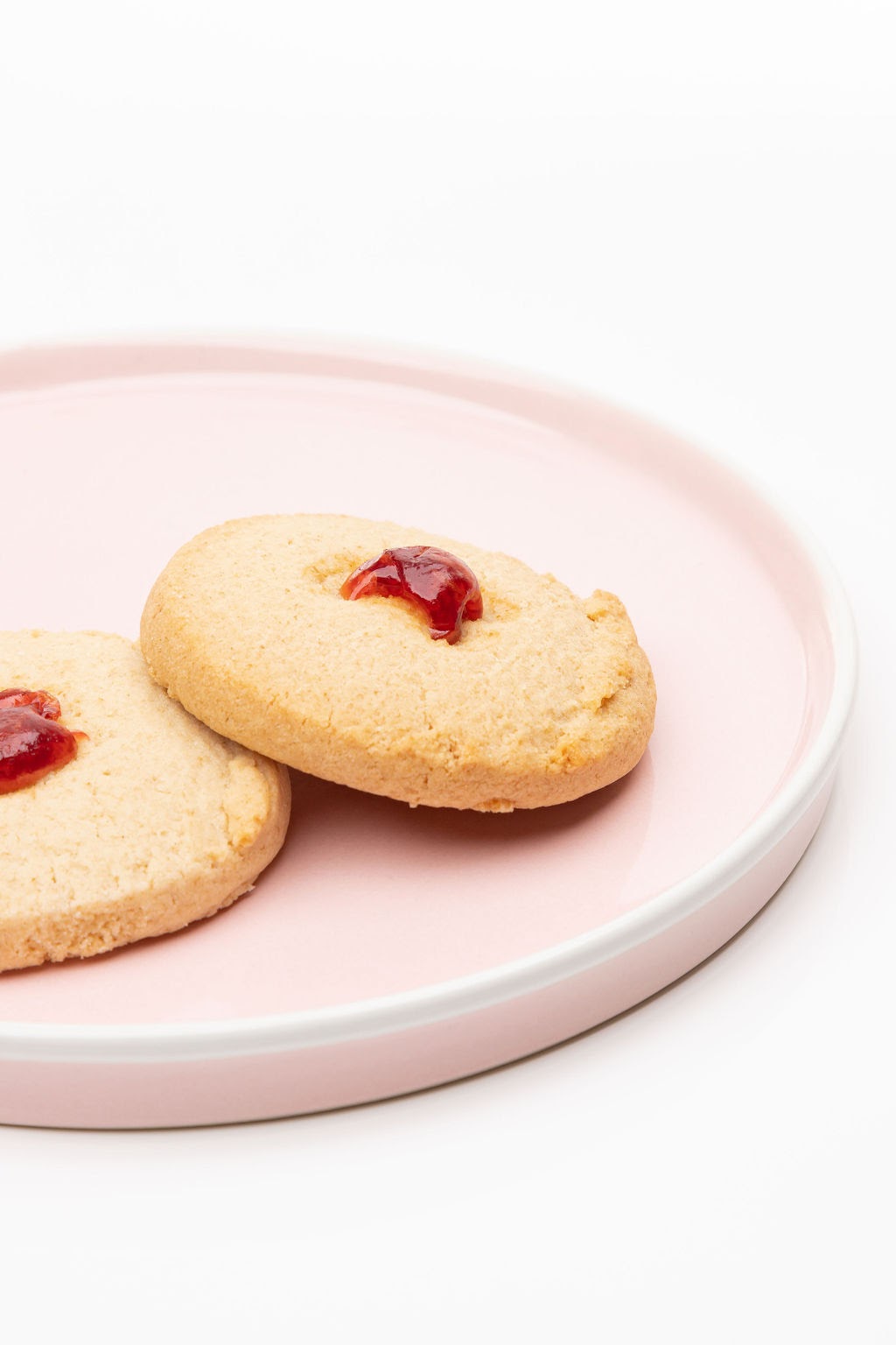 Two cookies with jam filling on a pink plate against a white background