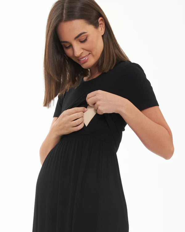 Pregnant Woman in a black maternity dress holding a beige nursing pad against a white background
