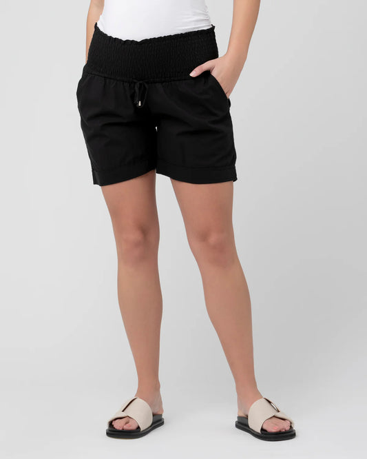 Pregnant woman wearing black maternity shorts on a plain background