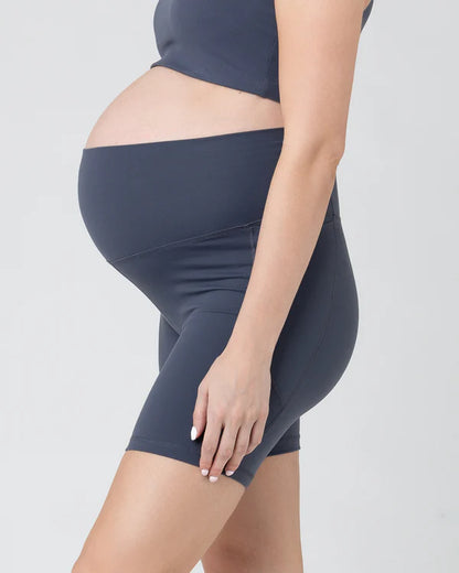 Pregnant woman wearing dark blue maternity shorts on a light gray background