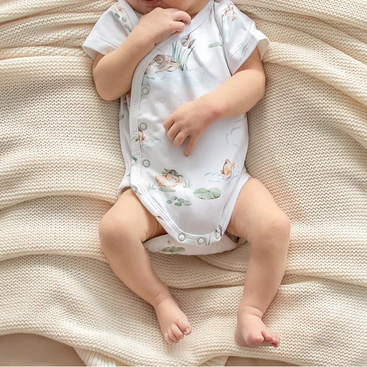 Newborn baby in a floral onesie lying on a soft beige blanket
