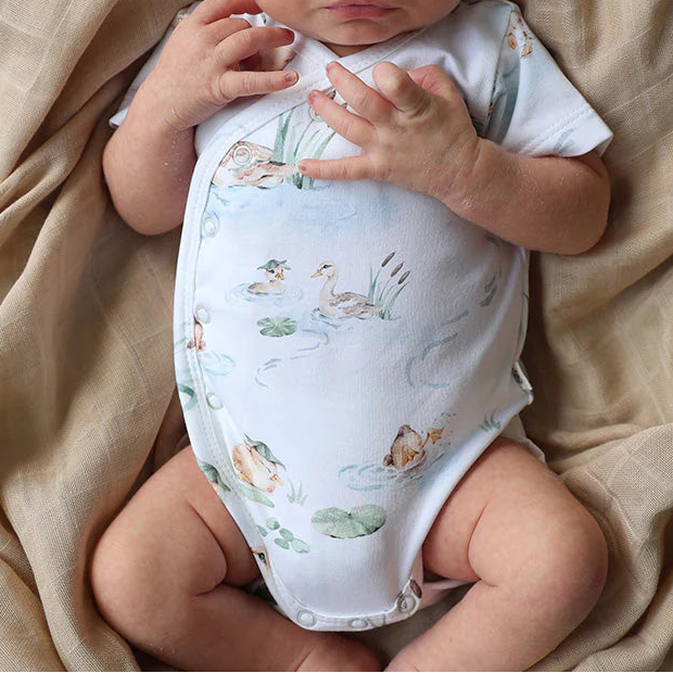 Newborn baby in a floral hat and romper lying on a beige blanket
