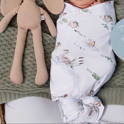 Newborn baby wrapped in a floral swaddle with a hat, lying on a green blanket next to a plush toy and 'hello world' sign.
