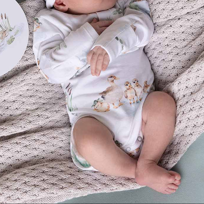 Newborn baby in a white onesie with animal prints, wearing a matching headband, lying on a textured blanket.