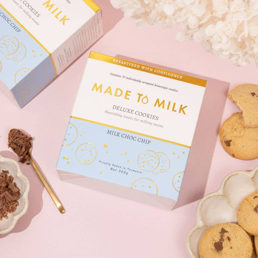 Box of 'Made to Milk' Deluxe Cookies with lactation cookies and chocolate on a pink background