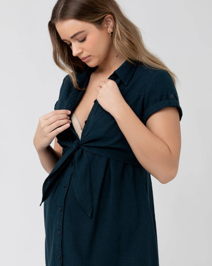 Pregnant Woman wearing a dark green dress with a knot detail on a light grey background