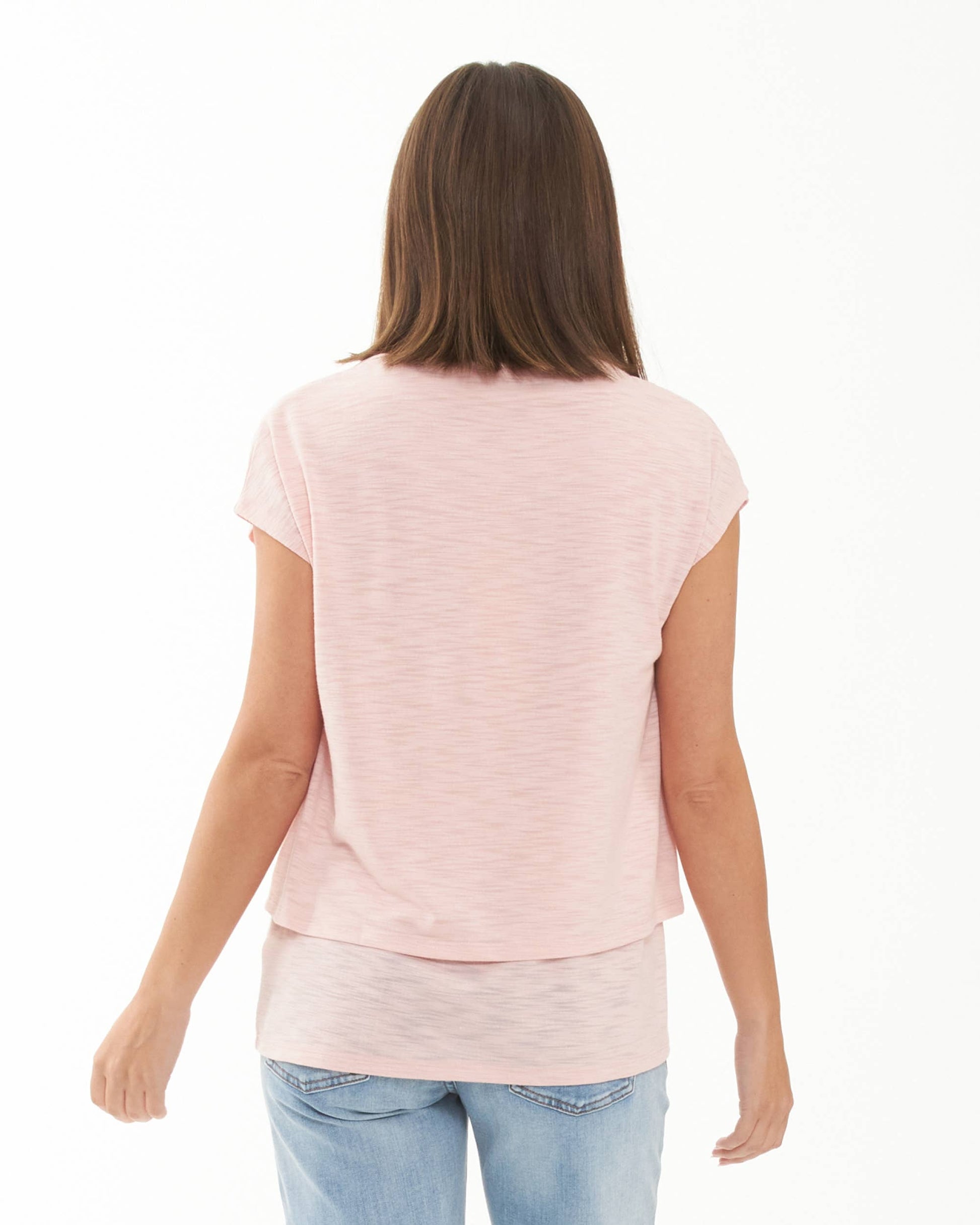 Pregnant Woman wearing a light pink layered top and blue jeans on a white background