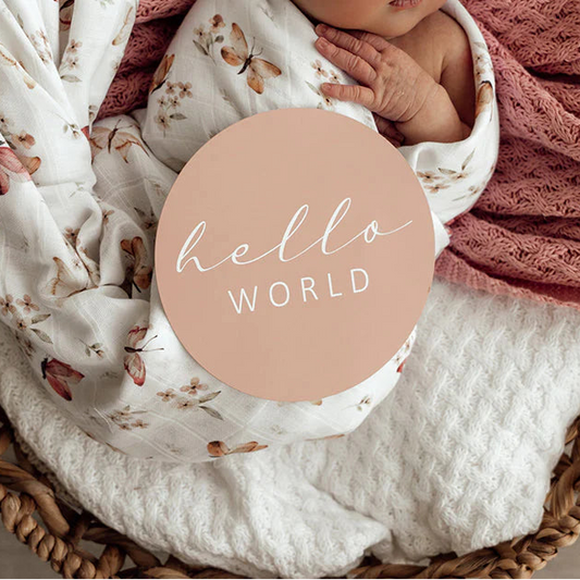 Newborn baby wrapped in a floral blanket with 'hello world' text in a wooden basket.