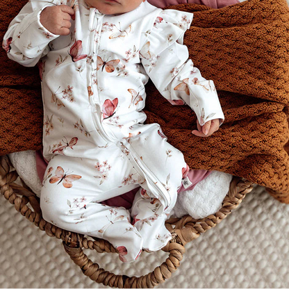 Newborn baby in a floral outfit and headband, wrapped in brown blanket, lying in a woven basket.