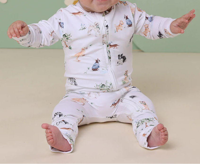 Baby wearing a patterned outfit with a headband, sitting on a beige surface with a green wall and floral decorations in the background.
