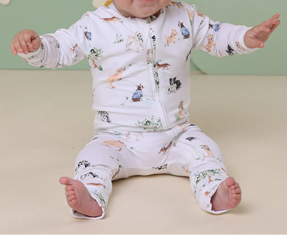 Baby wearing a patterned outfit with a headband, sitting on a beige surface with a green wall and floral decorations in the background.
