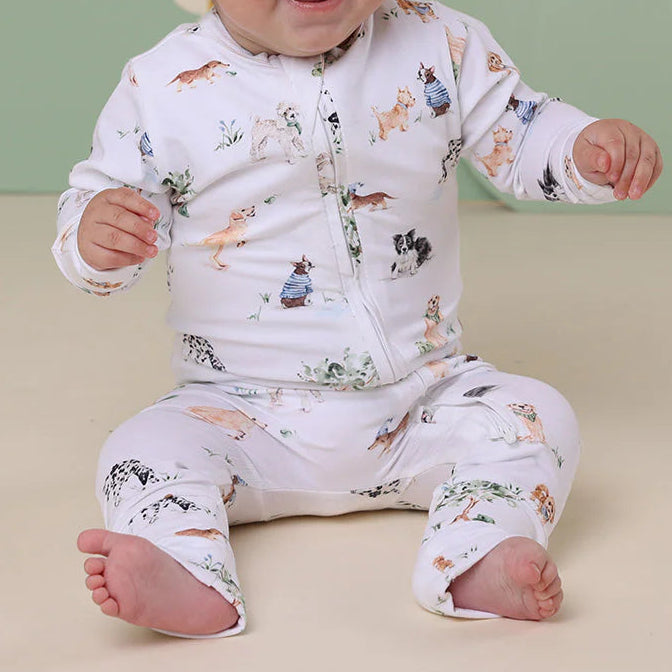 Baby wearing a white outfit with animal prints and a matching headband, sitting on a beige surface with a green background featuring flowers.