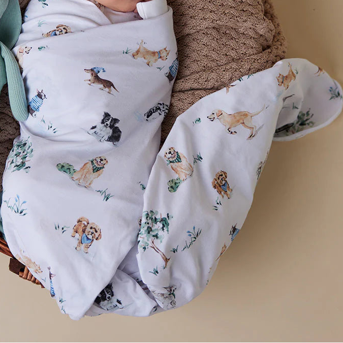 Newborn baby wrapped in a blanket with animal patterns, wearing a matching hat, in a wicker basket with a green toy.
