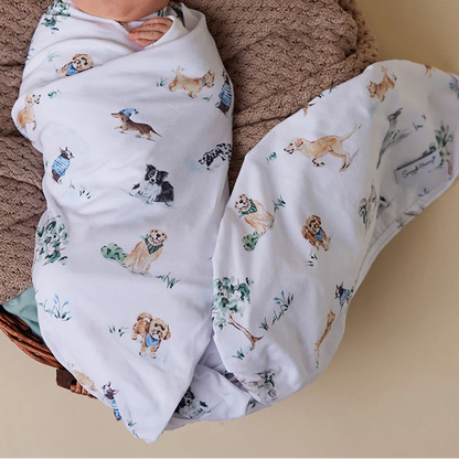 Newborn baby wrapped in a blanket with dog patterns, wearing a matching hat, in a wicker basket.