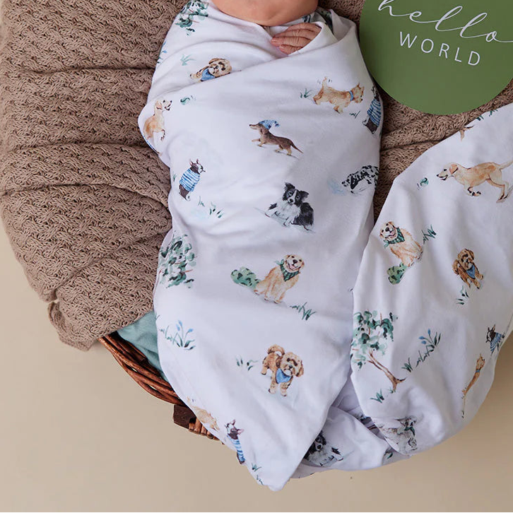 Newborn baby wrapped in a patterned blanket with a 'hello world' sign in the background