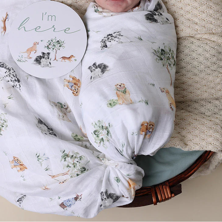 Newborn baby swaddled in a floral blanket with a 'I'm here' sign, lying on a textured surface.