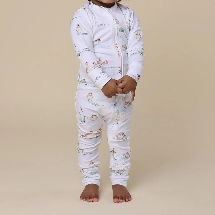 Child wearing a white onesie with animal prints on a beige background